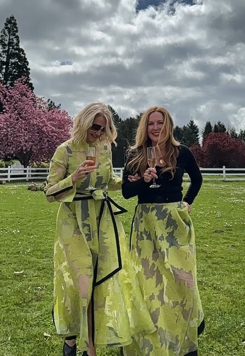 Two women in printed chartreuse dresses raising a toast on a bright lawn