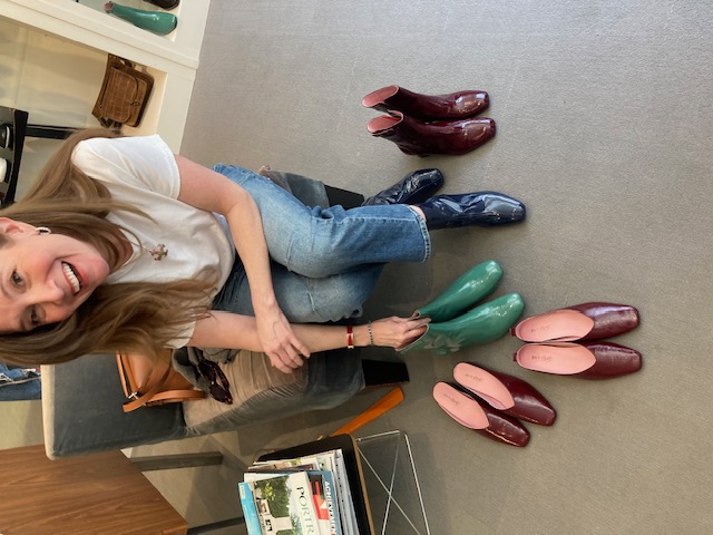 A smiling customer with an array of colorful boots and flats arranged on the floor at Zelda's