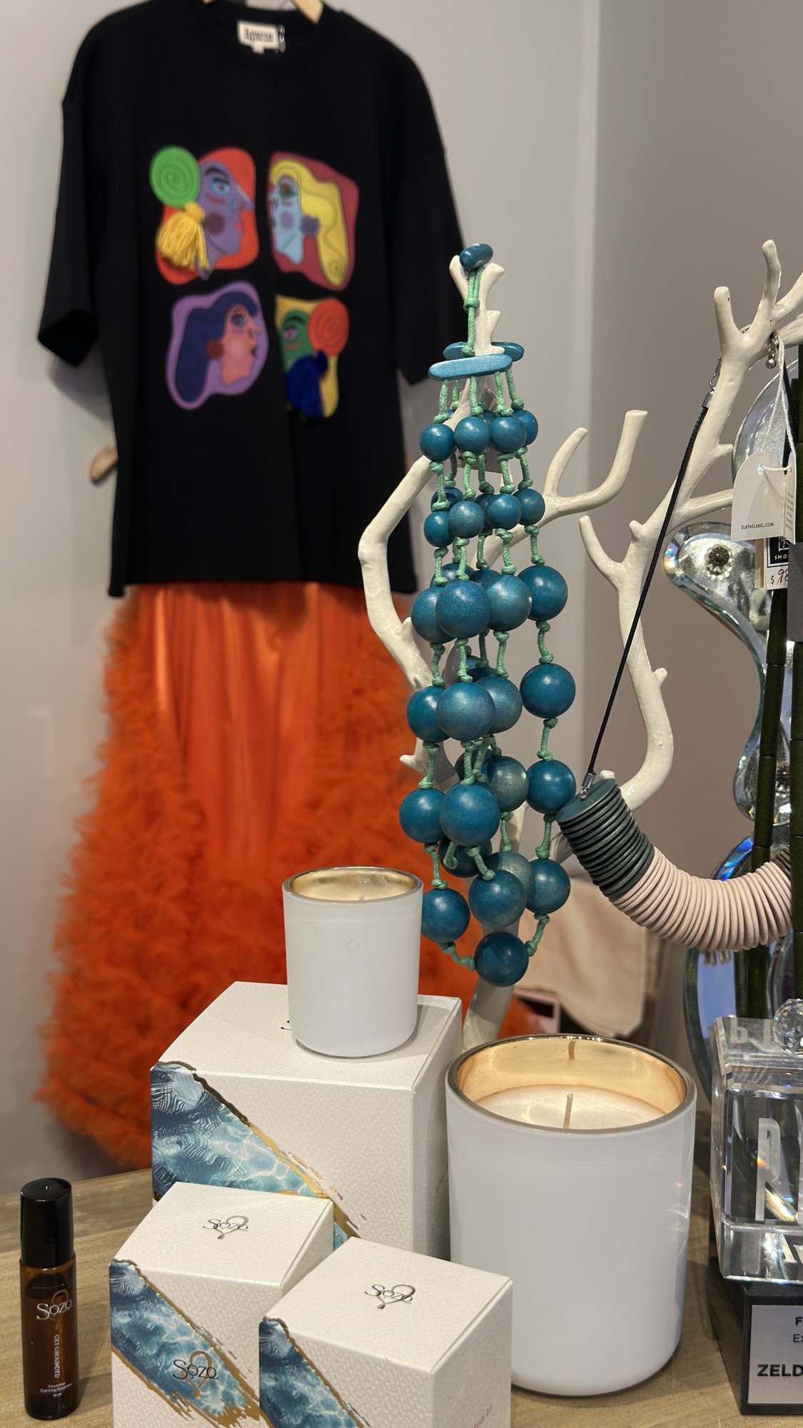 A graphic tee, beaded necklace and candles on display at Zelda's