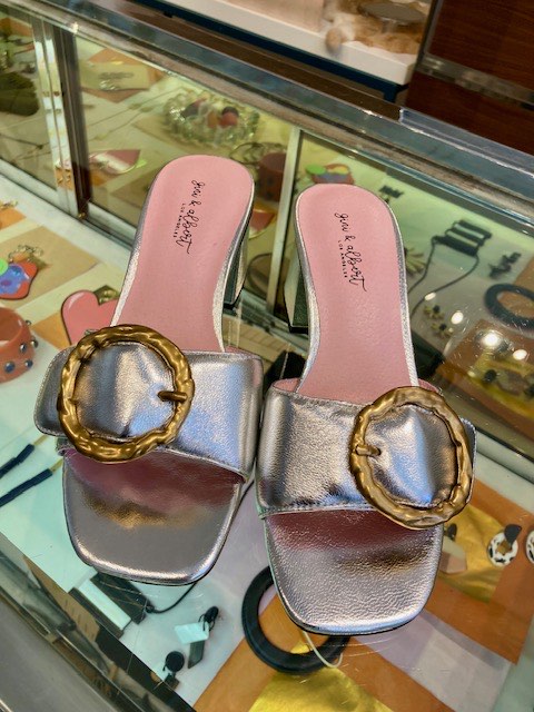 Silver metallic sandals with woven gold buckles in the display case at Zelda's