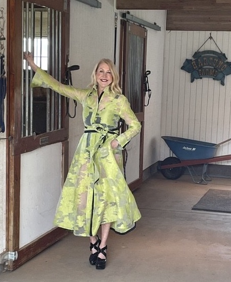 A woman posing in a chartreuse patterned dress in the doorway of a stable