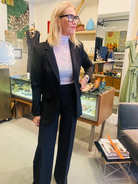 A customer trying a black blazer and pinstripe trousers with a statement necklace at Zelda's