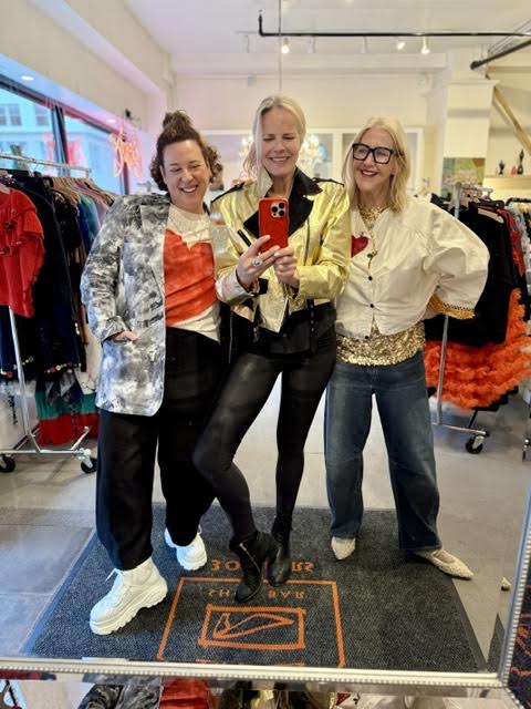 Three women in statement jackets posing together for a mirror photo inside Zelda's