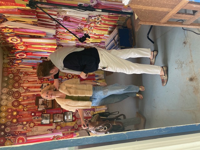 Two women styling a cropped shearling jacket against a wall of prize ribbons