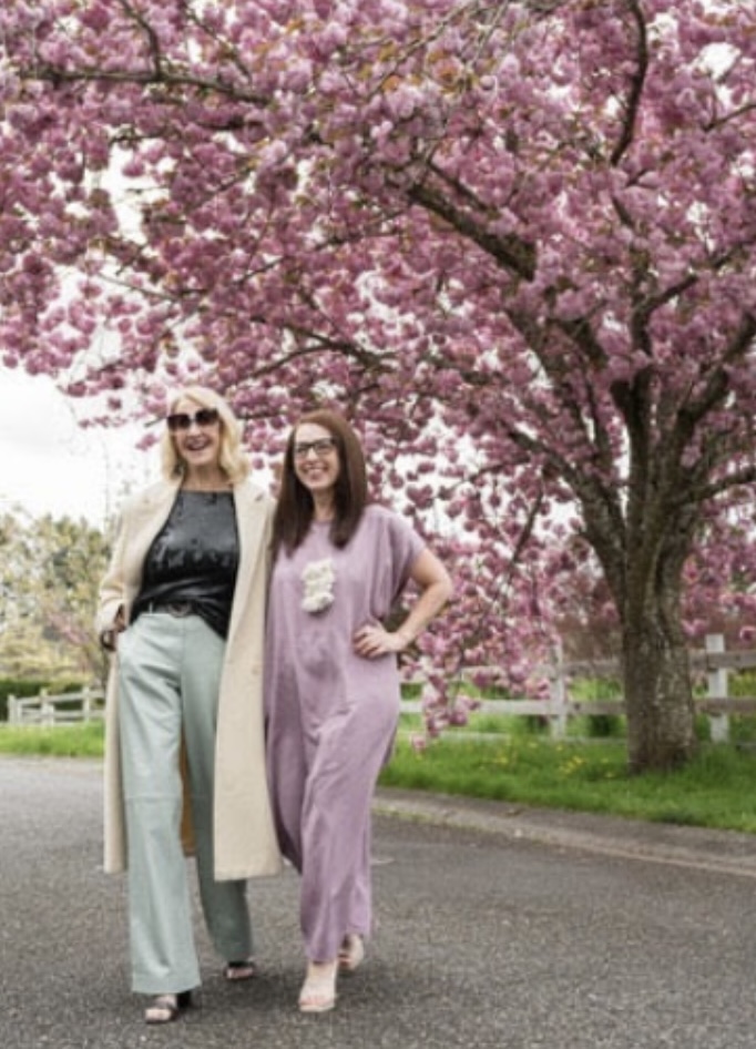 Two customers in tailored trousers and an olive jumpsuit beneath a blooming cherry tree